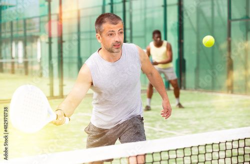 Athletic mens plays padel. View through the tennis net © JackF