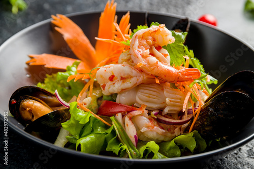 Salad with seafood and vegetables on black bowl on dark stone table, Chinese cuisine macro close up