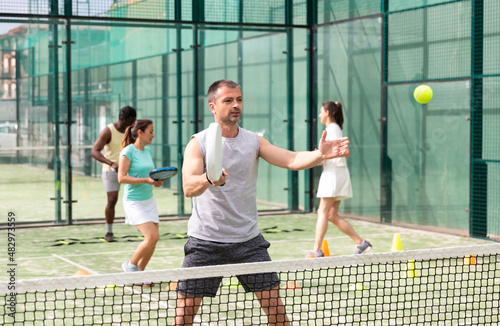 Portrait of man paddle tennis player performing basic strokes technique at court during group training © JackF