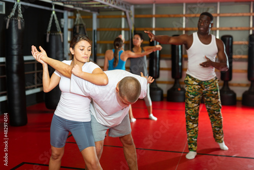 Latino woman is training with man on the self-defense course in gym