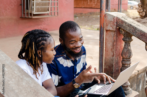 two young african friends, male and female watching movie with a laptop