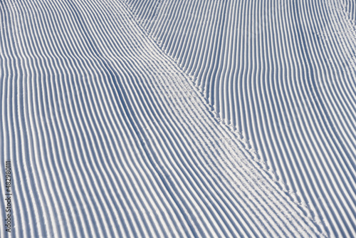 Fresh snowfall after the groomers have finished rolling the ski slopes, pattern and texture in a natural cold white snow background 