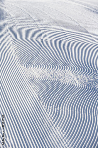 Fresh snowfall after the groomers have finished rolling the ski slopes, pattern and texture in a natural cold white snow background 