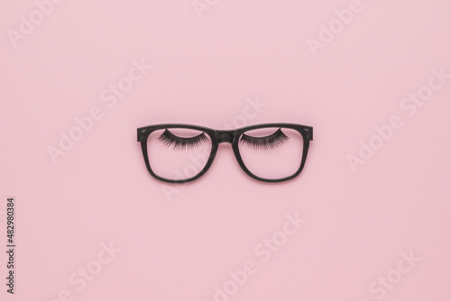 Classic black glasses with large eyelashes on a light pink background. Minimalism.