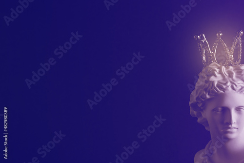 A plaster statue with a crown on a dark background. Tinted image.