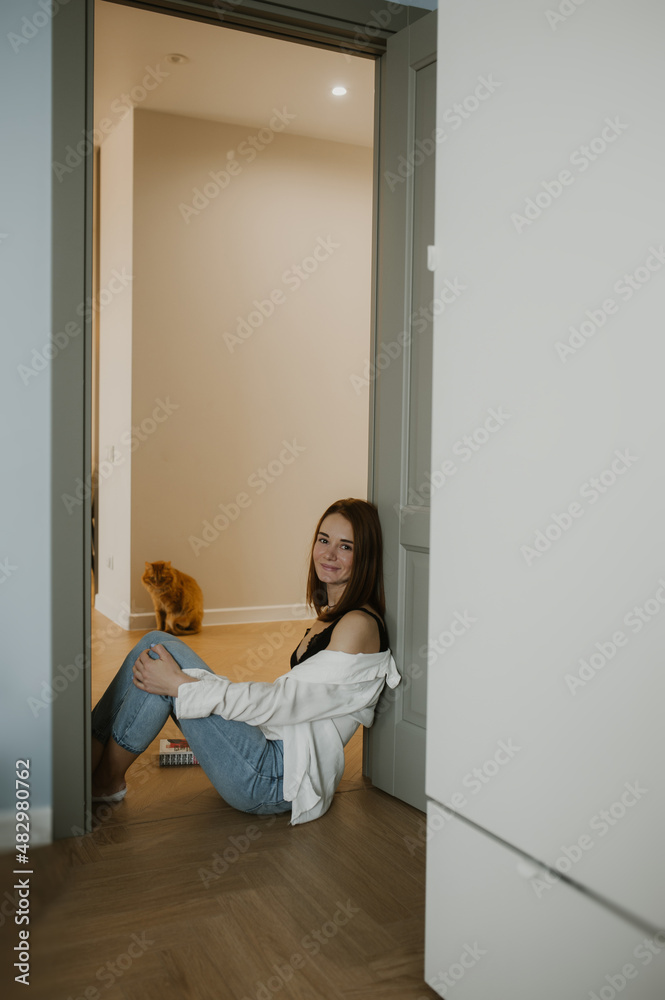 young slender woman with red hair, crop top and jeans sitting on floor with pet in scandi apartment scandi modern style. cozy atmosphere at home. vertically, selective focus young slender woman with red hair, crop top and jeans sitting on floor with pet in scandi apartment scandi modern style. cozy atmosphere at home. vertically, selective focus