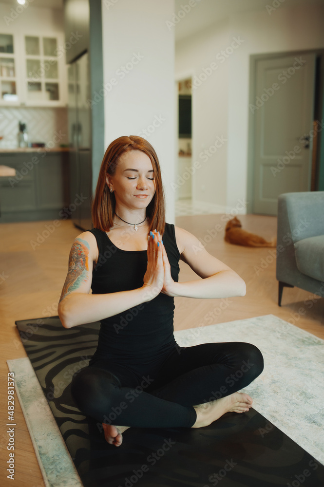 young woman with bright red hair does yoga in stylish modern apartment. woman slender muscular body . yoga basic asanas. home independent training. selective focus, vertically young woman with bright red hair does yoga in stylish modern apartment. woman slender muscular body . yoga basic asanas. home independent training. selective focus, vertically