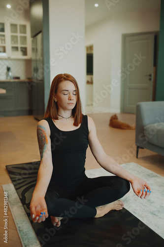 Fototapeta Naklejka Na Ścianę i Meble -  young woman with bright red hair does yoga in stylish modern apartment. woman slender muscular body . yoga basic asanas. home independent training. selective focus, vertically