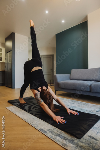 young woman with bright red hair does yoga in stylish modern apartment. woman slender muscular body . yoga basic asanas. home independent training. selective focus, vertically photo