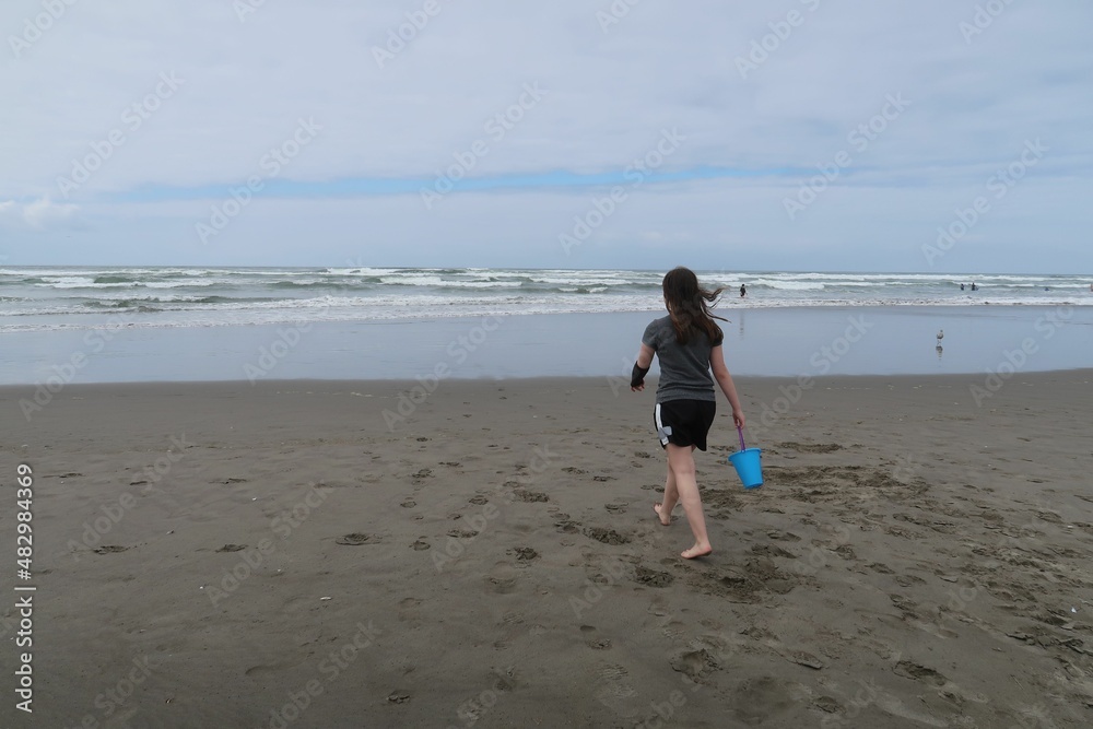 Girl Walking Towards the Ocean with a Bucket