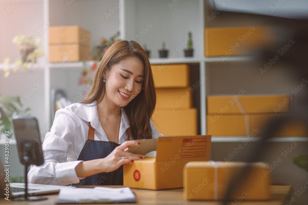 Startup SME small business entrepreneur SME or freelance Asian woman using a laptop with box, Young success Asian woman with her hand lift up, online marketing packaging box and delivery, SME concept. Startup SME small business entrepreneur SME or freelance Asian woman using a laptop with box, Young success Asian woman with her hand lift up, online marketing packaging box and delivery, SME concept.