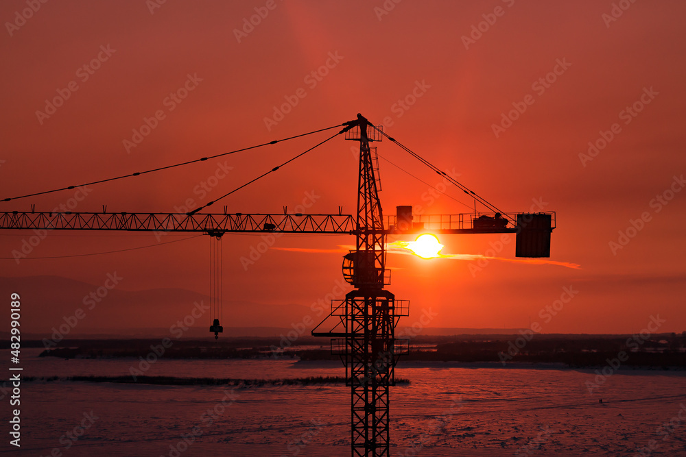 silhouette of tower crane with the sun behind it during the orange sunset