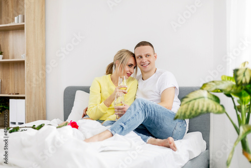 A young couple in the bedroom with glasses of wine and flowers celebrating Valentine's Day or anniversary