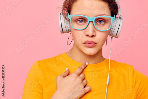 funny girl wearing blue glasses listening to music on headphones pink background unaltered