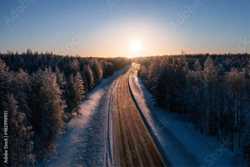 Road leading towards sunset through snowy boreal forest. Transportation and landscapes in Finland
