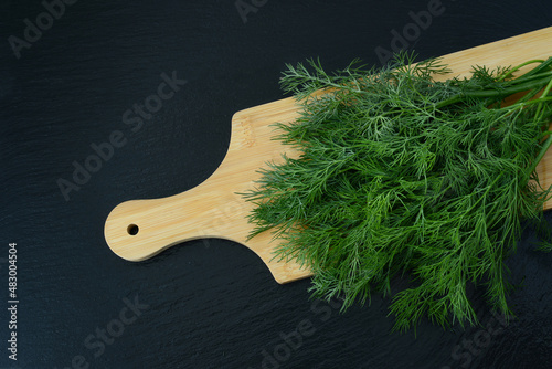 Bunch of dill or fennel on a wooden cutting board on black background, top view. Aromatic seasoning