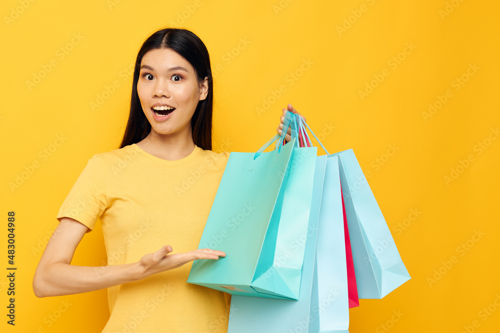 Portrait Asian beautiful young woman in a yellow T-shirt with multicolored shopping bags studio model unaltered Portrait Asian beautiful young woman in a yellow T-shirt with multicolored shopping bags studio model unaltered