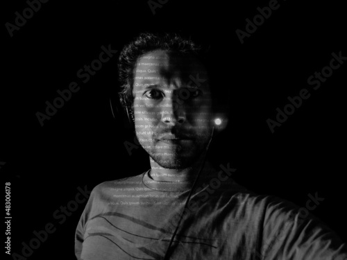 A man with letters projected on his face in a dark room