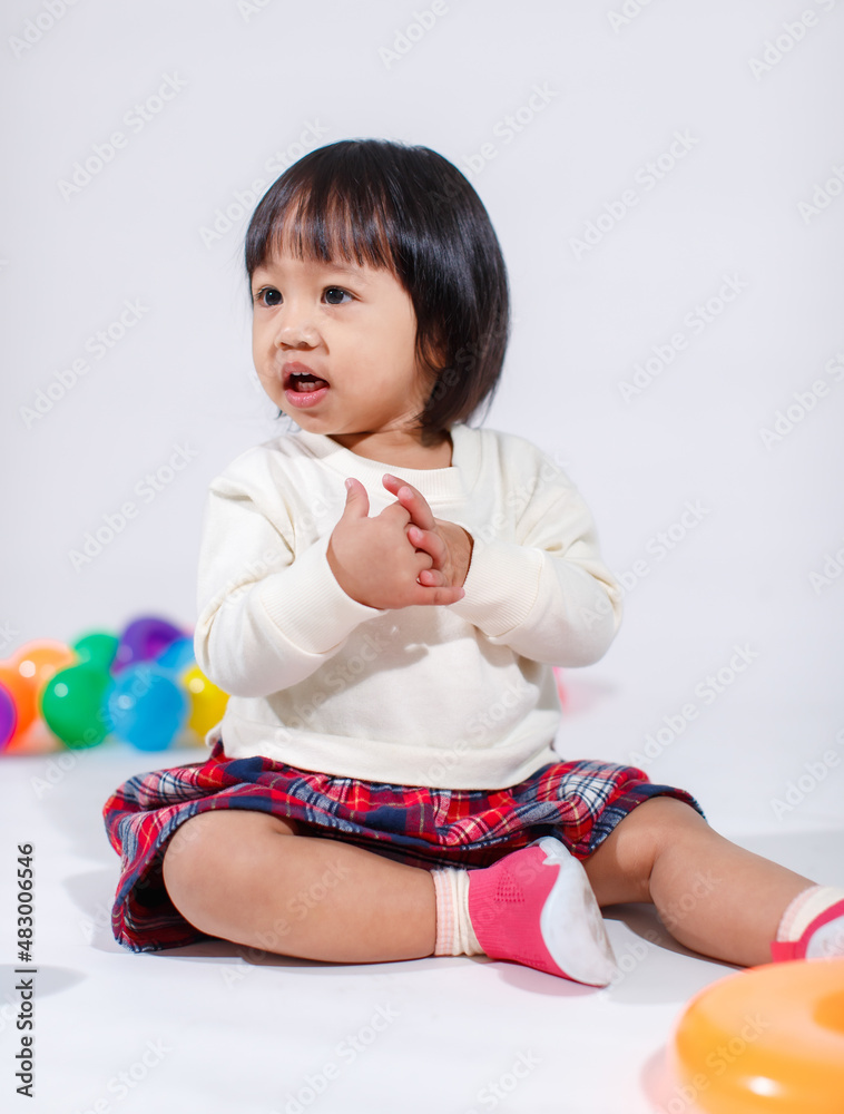 Studio shot of little cute short black hair Asian baby girl daughter model in casual plaid skirt sitting on floor smiling laughing playing with colorful round balls toy alone on white background Studio shot of little cute short black hair Asian baby girl daughter model in casual plaid skirt sitting on floor smiling laughing playing with colorful round balls toy alone on white background