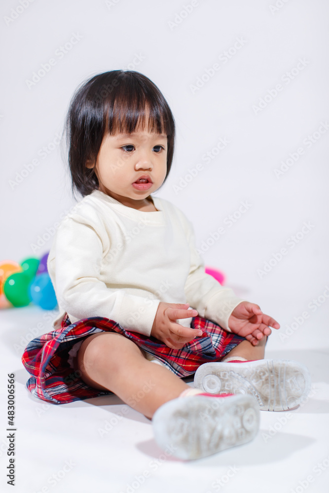 Studio shot of little cute short black hair Asian baby girl daughter model in casual plaid skirt sitting on floor smiling laughing playing with colorful round balls toy alone on white background Studio shot of little cute short black hair Asian baby girl daughter model in casual plaid skirt sitting on floor smiling laughing playing with colorful round balls toy alone on white background