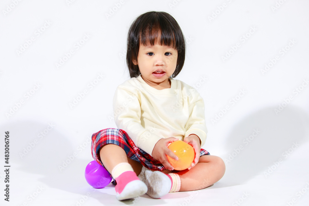 Studio shot of little cute short black hair Asian baby girl daughter model in casual plaid skirt sitting on floor smiling laughing playing with colorful round balls toy alone on white background Studio shot of little cute short black hair Asian baby girl daughter model in casual plaid skirt sitting on floor smiling laughing playing with colorful round balls toy alone on white background