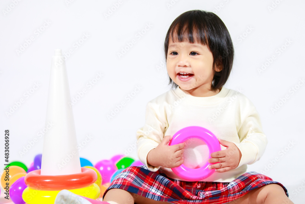 Studio shot of little cute Asian baby girl daughter model in casual outfit sitting on floor holding playing with colorful plastic rings construction pyramid toy and small balls on white background Studio shot of little cute Asian baby girl daughter model in casual outfit sitting on floor holding playing with colorful plastic rings construction pyramid toy and small balls on white background