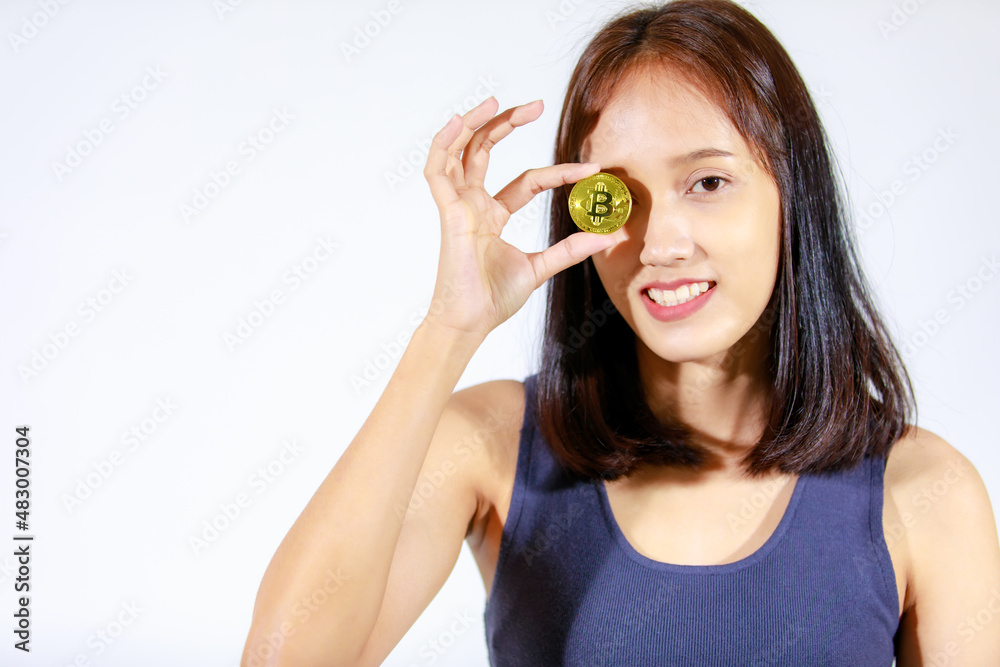 Portrait isolated closeup studio cutout shot of Asian young rich wealthy female teenager model in tank top shirt smiling look at camera showing golden bitcoin coin money in hand on white background Portrait isolated closeup studio cutout shot of Asian young rich wealthy female teenager model in tank top shirt smiling look at camera showing golden bitcoin coin money in hand on white background