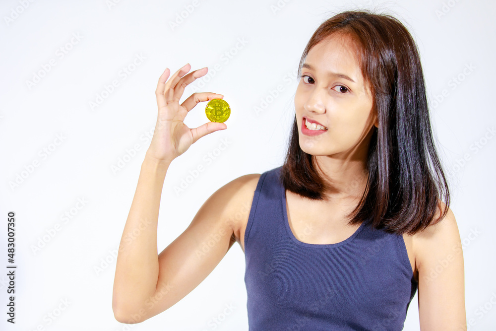 Portrait isolated closeup studio cutout shot of Asian young rich wealthy female teenager model in tank top shirt smiling look at camera showing golden bitcoin coin money in hand on white background Portrait isolated closeup studio cutout shot of Asian young rich wealthy female teenager model in tank top shirt smiling look at camera showing golden bitcoin coin money in hand on white background