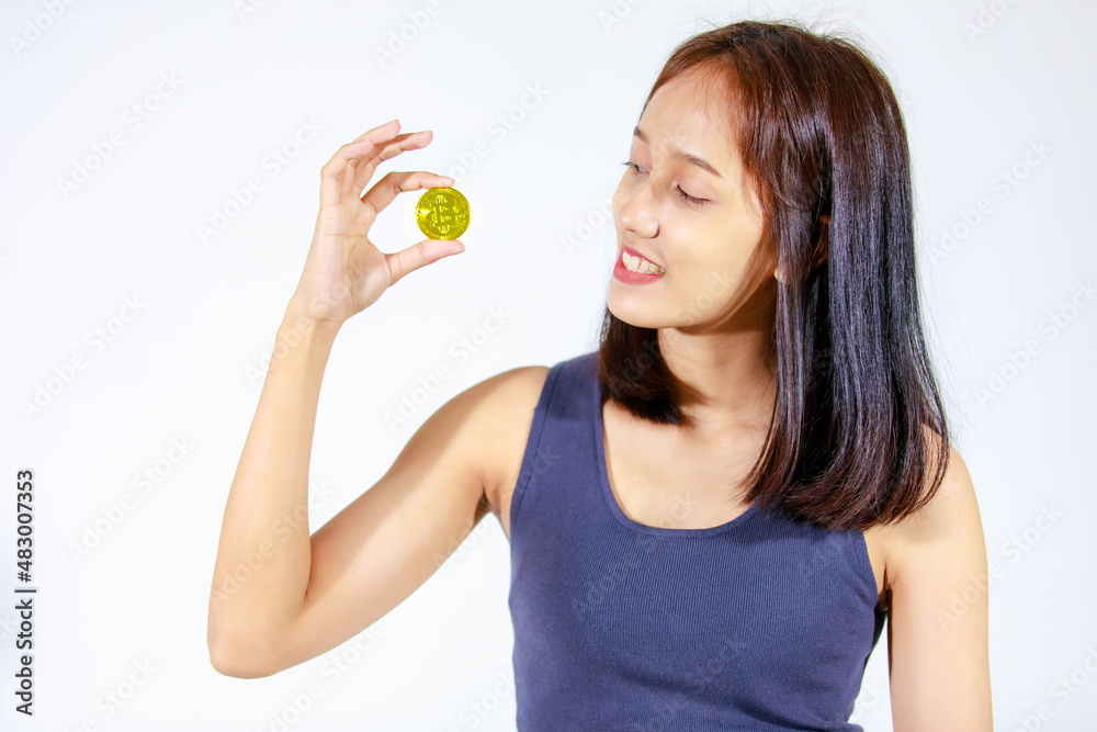 Portrait isolated closeup studio cutout shot of Asian young rich wealthy female teenager model in tank top shirt smiling look at camera showing golden bitcoin coin money in hand on white background Portrait isolated closeup studio cutout shot of Asian young rich wealthy female teenager model in tank top shirt smiling look at camera showing golden bitcoin coin money in hand on white background