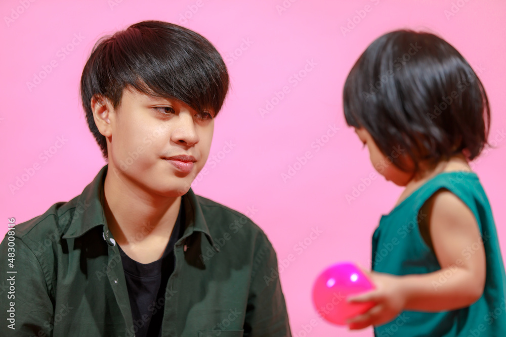 Portrait closeup studio shot of young happy Asian family father and little cute baby girl daughter sitting on floor together smiling look at camera holding colorful balloons on pink background Portrait closeup studio shot of young happy Asian family father and little cute baby girl daughter sitting on floor together smiling look at camera holding colorful balloons on pink background