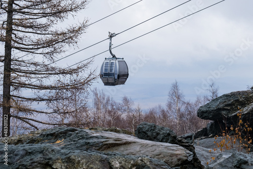 A modern cable car rides into the mountains, with a blue cloudy sky in the background. Beautiful view of the cable car in autumn.