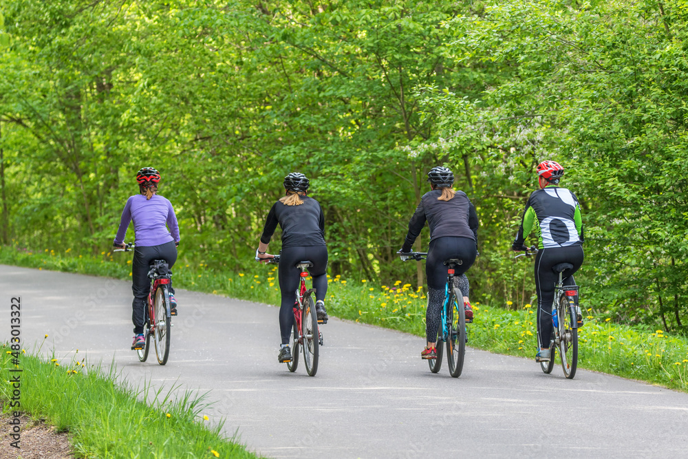 Fototapeta premium Young women exercising on bikes in a road in a deciduous forest