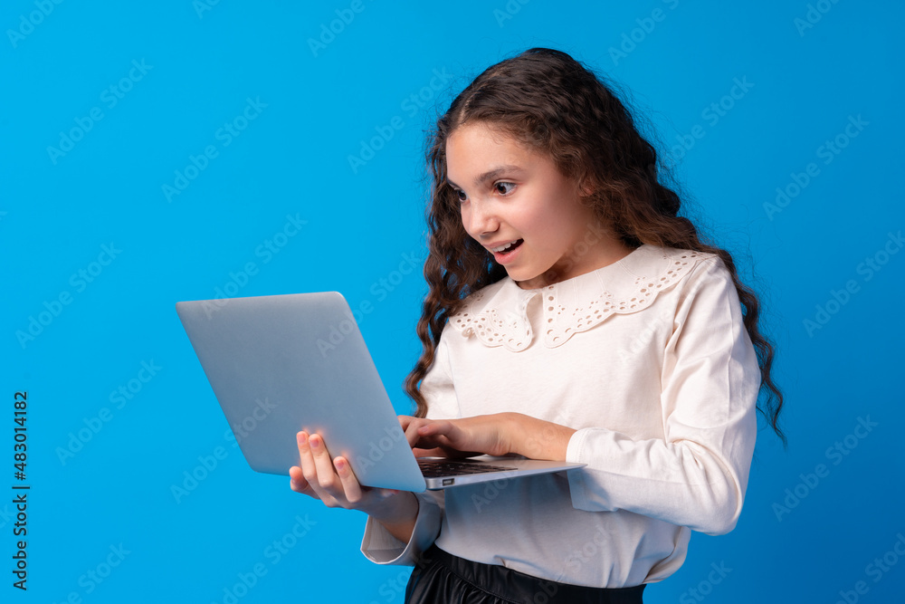 Portrait of a little girl holding laptop computer while standing against blue background