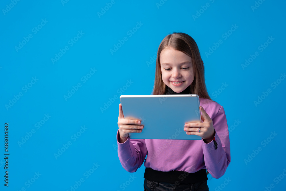 Little girl uses a digital tablet on a blue background Little girl uses a digital tablet on a blue background