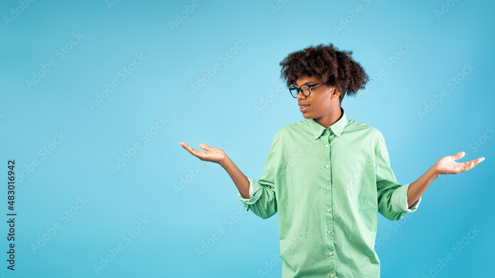 Making choice. Teen black guy making scales with his empty hands, standing over blue background, free space Making choice. Teen black guy making scales with his empty hands, standing over blue background, free space
