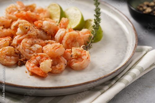 Grilled shrimps or tiger prawns served with lime, garlic and fresh herbs on scandi round plate on concrete surface. Pescatarian protein nutrition