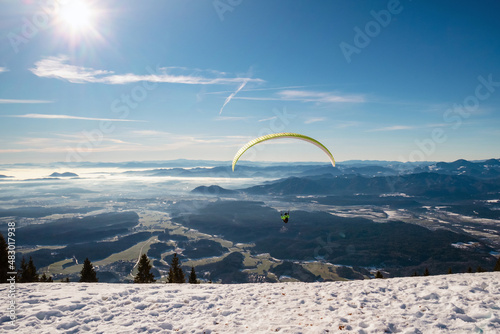 Paragliding in mountains, winter time with snow and blue sunny sky.