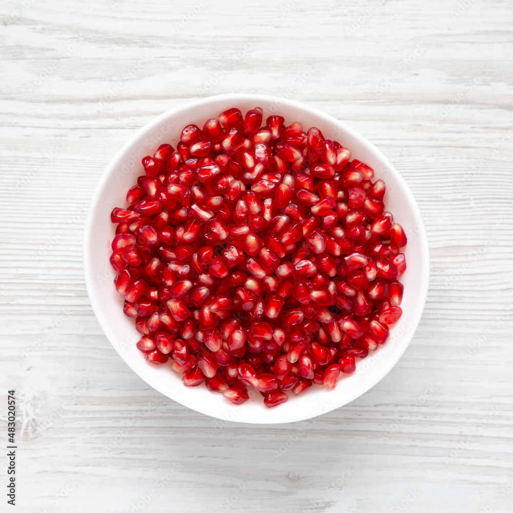 Red Pomegranate Seeds in a Bowl on a white wooden surface, top view. Flat lay, overhead, from above. Red Pomegranate Seeds in a Bowl on a white wooden surface, top view. Flat lay, overhead, from above.