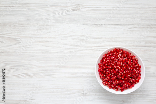 Red Pomegranate Seeds in a Bowl on a white wooden background, top view. Flat lay, overhead, from above. Space for text.