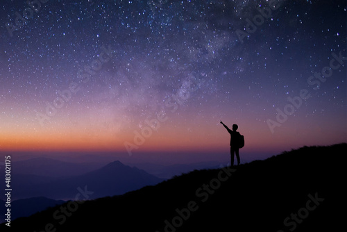 Silhouette of young man standing and open arms watched the star  milky way and night sky alone on top of the mountain. He enjoyed traveling and was successful when he reached the summit.