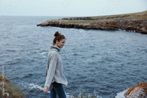 woman in a gray sweater stands on a rocky shore nature female relaxing
