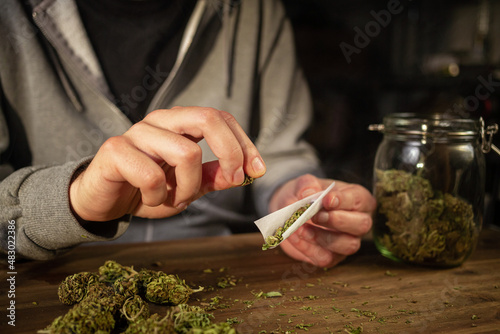 Photography Man rolling marijuana cannabis joint in coffee shop Amsterdam with CBD weed buds in glass jars