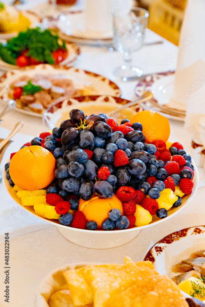 a bowl of berries and fruits on the festive table. tangerines, pineapples, raspberries, blueberries and grapes. delicious and healthy dessert. vegetarianism. a bowl of berries and fruits on the festive table. tangerines, pineapples, raspberries, blueberries and grapes. delicious and healthy dessert. vegetarianism.