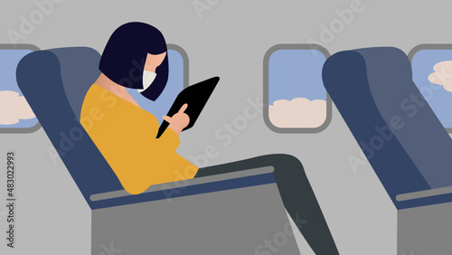 Female passenger wearing protective mask  uses tablet onboard the aircraft