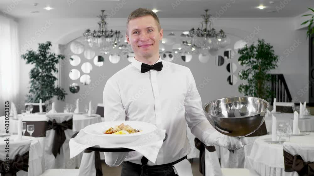 Male waiter opens the lid of a tray with a hot dish