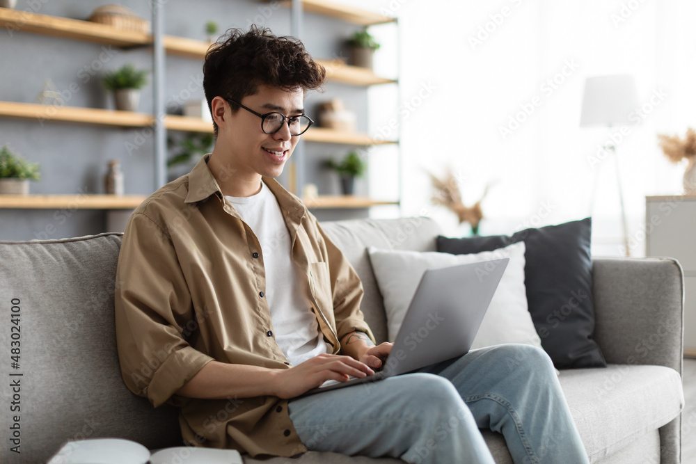 Smiling asian man working on laptop at home Smiling asian man working on laptop at home
