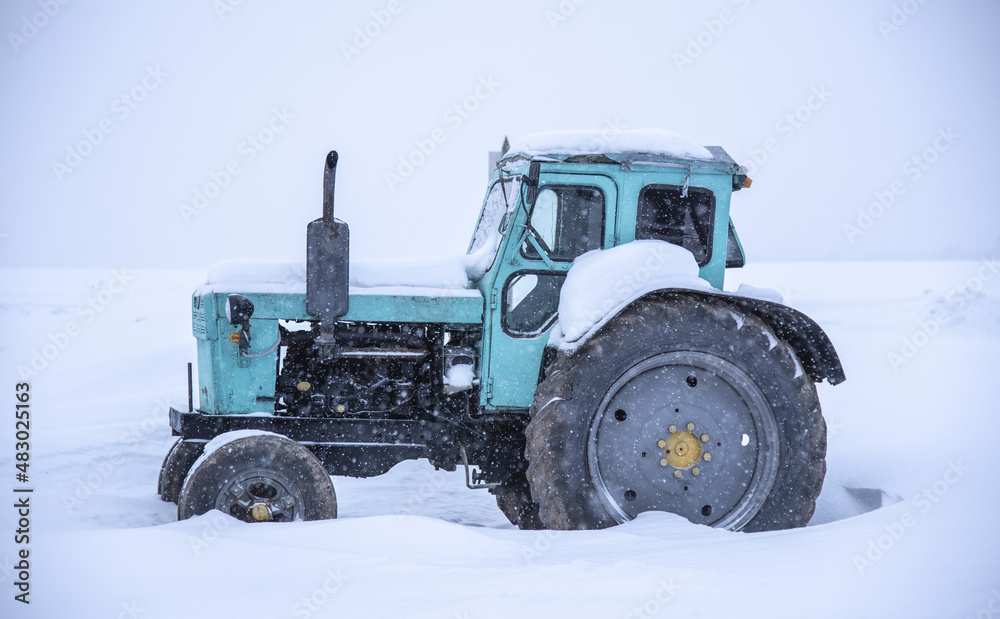 Tractor on a deserted snow-covered field against a cloudy sky. Tractor on a deserted snow-covered field against a cloudy sky.