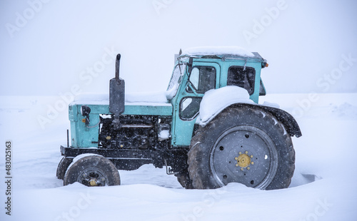 Tractor on a deserted snow-covered field against a cloudy sky.