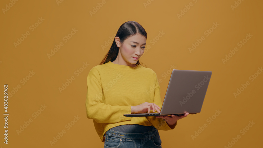 Young adult typing on laptop pc with technology in studio. Asian woman using portable computer to browse internet, advertising freelance work and modern communication on device. Young adult typing on laptop pc with technology in studio. Asian woman using portable computer to browse internet, advertising freelance work and modern communication on device.