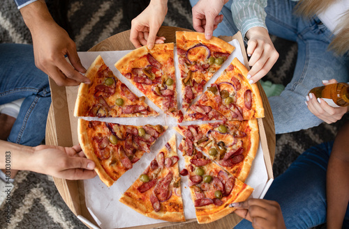 Top view of friends taking pieces of tasty pizza with sasuages, drinking beer, having party, cropped